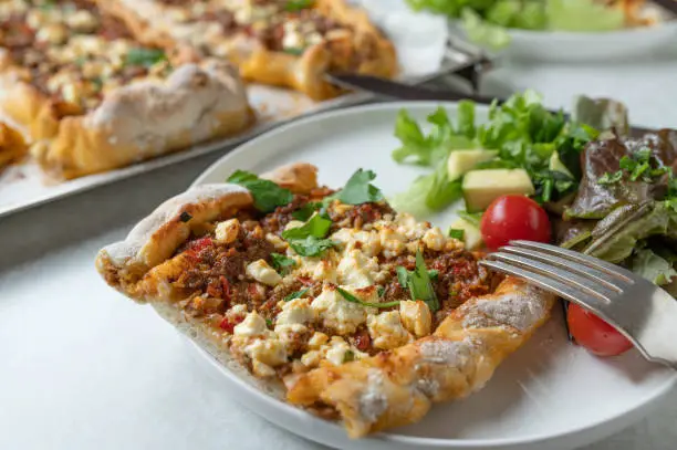 Homemade turkish pide or turkish flatbread baked with yeast dough and topped with spicy ground beef, tomatoes, peppers, onion, garlic and parsley