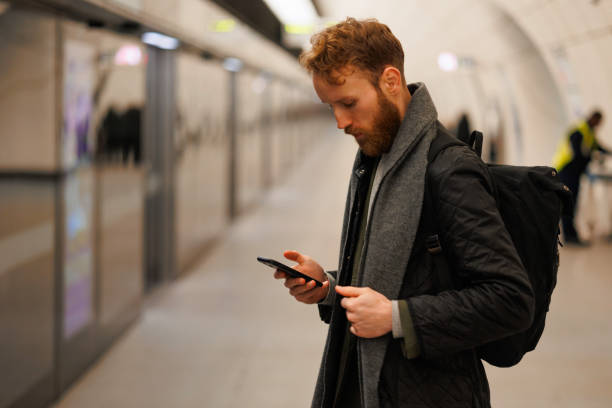 istock Man using smartphone on the platform of the subway station while waiting for the train 1472478374