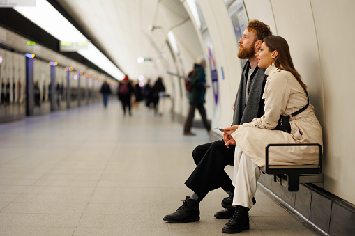 Couple man and woman sitting on a bench in a subway station waiting for their train