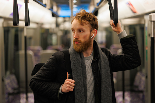 Man in wireless headphones and with a backpack is standing in a subway train