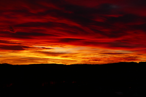 A golden Sun turns the early morning sky red as it breaks through clouds on Queensland's Gold Coast. The Pacific Ocean and horizon can be seen at the very bottom of frame.  Die to the composition and colour of the sky, this image could be used to address an range of topics and themes including holidays, seasons, time of day, climate change or environment.