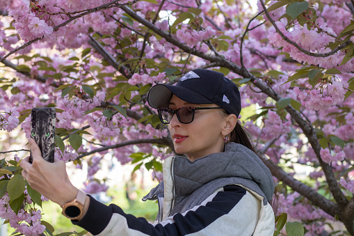 Woman takes a self photo against of blossom sakura on mobilephone. Smartphone shot japanese cherry tree. Pink flowers and youngwoman on the screen. Snapshot on cellphone.