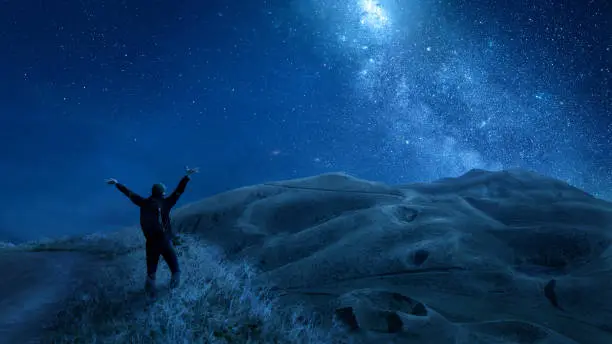 Woman with raised arms looking at a stunning night sky with stars and galaxies.