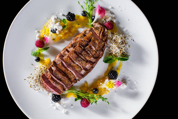 istock Grilled cut duck breast, with jam, blackberries, raspberries, currants, mint, young shoots, flower petals on a white plate and dark background. Horizontal orientation 1472496542