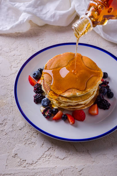 istock Pancakes with maple syrup, blueberries, strawberries, blackberries in a plate on rough concrete with a cloth in the background and a bottle pouring over the food 1472498229