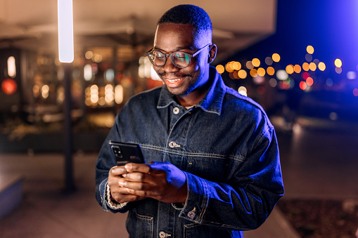 Young man is texting message on smart phone outdoors at night