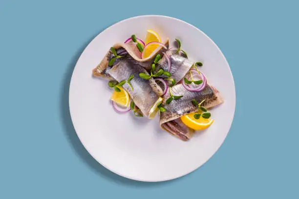 Herring fillet with mung bean salad, lemon and onion in a plate on a blue background