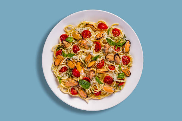 Spaghetti with mussels, cheese, tomatoes and basil in a plate on a blue background
