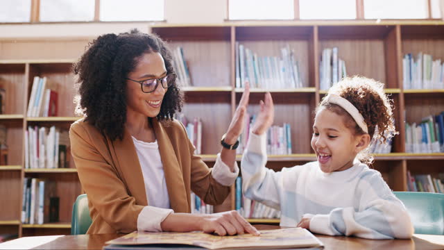 High five, teacher and helping a girl with reading, education and studying at a school. Success, goal and woman giving motivation to a student learning to read a book in a library with support