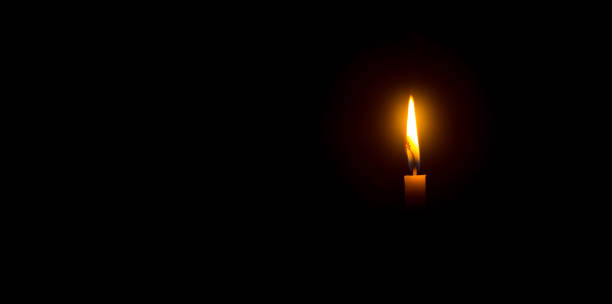 istock A single burning candle flame or light glowing on an orange candle on black or dark background on table in church for Christmas, funeral or memorial service with copy space 1472503931