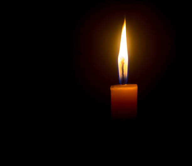 istock A single burning candle flame or light glowing on an orange candle on black or dark background on table in church for Christmas, funeral or memorial service with copy space 1472503949