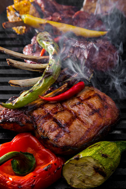 istock Grilled beef steak on the bone with spices, garlic, zucchini, pepper and corn on burning coals with smoke. Horizontal orientation 1472507474