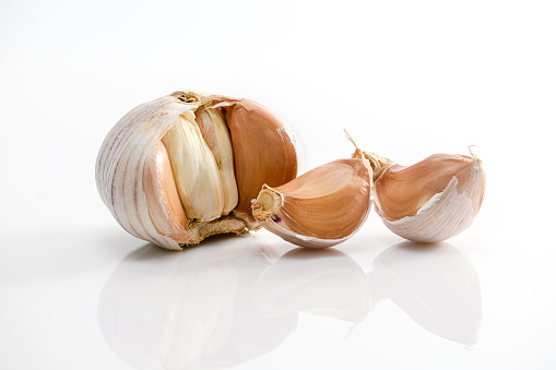 Stock photo showing close-up of a stack of fresh, whole garlic bulbs on a mottled black plate, against a mottled green garden background.