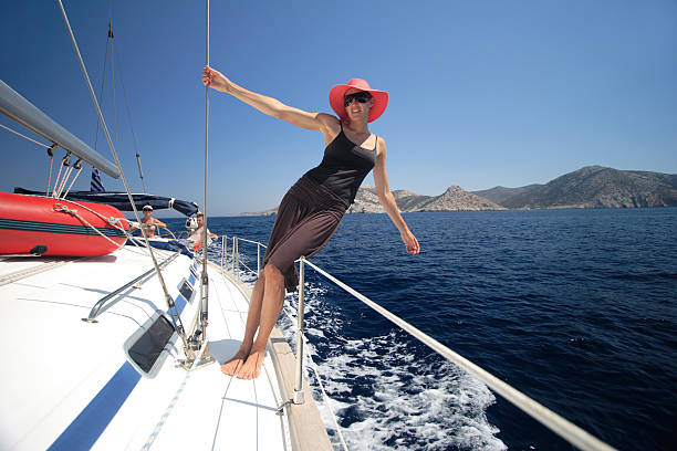 A young athletic women hangs off the shrouds of a yacht sailing the Cyclades Islands in Greece