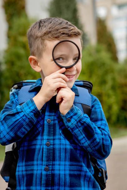 istock Schoolboy looking through a magnifying glass, with a surprised expression, squinting his eyes 1472509056
