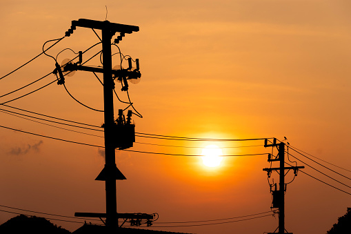 Silhouette electric post with cable wires against orange sunset sky background