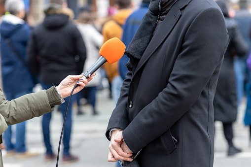 Reporter holding microphone making media interview with male politician or business person. Street interview or vox popoli concept.