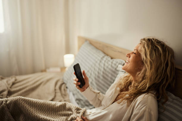 istock Cheerful woman using mobile phone in a bed. 1472512613