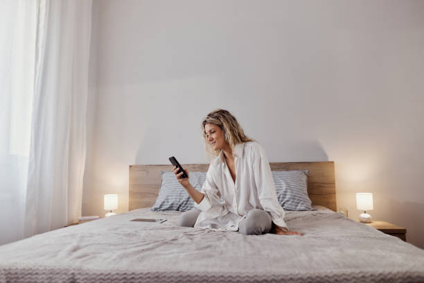 istock Young woman text messaging on cell phone on a bed. 1472512846