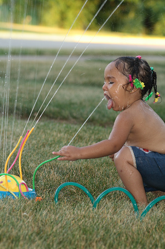 A toddler getting a drink from her sprinkler