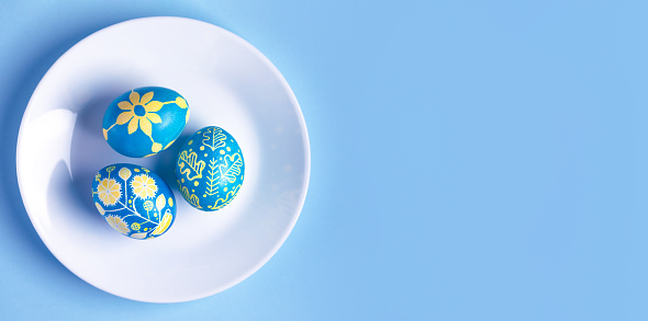 Easter eggs on white plate and painted with Ukrainian national colors, blue and yellow, and depicting Ukrainian ornament
