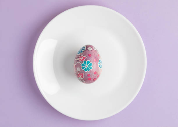 istock Pysanka on blue plate against lilac background 1472517506