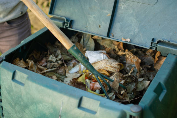 A young man is mixin the organic waste throwed to the outdoor compost bin.The compost bin is placed in a home garden to recycle organic waste produced in home and garden and produce organic fertilizer. Concept of recycling and sustainability un joven está mezclando los desechos orgánicos arrojados al contenedor de compost al aire libre. el contenedor de compost se coloca en un jardín casero para reciclar los desechos orgánicos producidos en el hogar y el jardín y producir fertilizante org