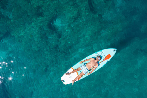 istock Drone view of man lying on a stand up paddle 1472519830