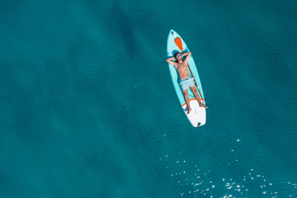 istock Drone view of man lying on a stand up paddle 1472520587