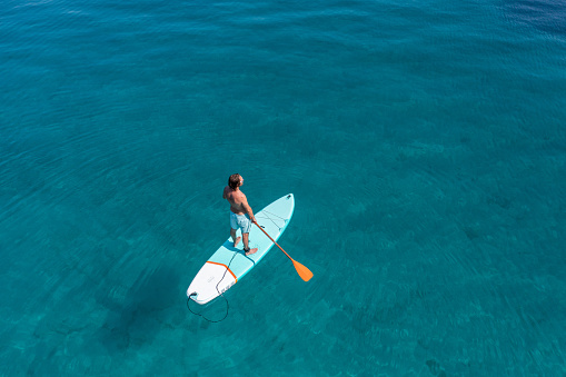 He stands on paddle board and enjoys relaxation on tropical turquoise lagoon