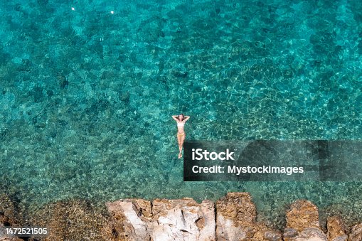 istock Woman floating on turquoise sea, she enjoys her summer vacations, sun shining and clear water 1472521505