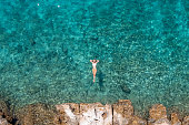 Woman floating on turquoise sea, she enjoys her summer vacations, sun shining and clear water