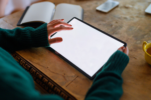 Woman holding and touching blank white screen of digital tablet on desk