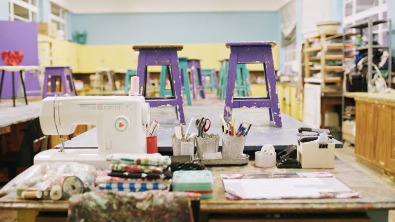 Art, class with desk and table in empty classroom, creativity and painting lesson, design and artistic. Creative education, teaching and learning, paint and sewing machine on desk in workspace