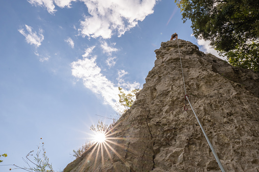 She explores new climbing places in Croatia.\nLow angle view, sunbeam on the rock. She moves upward towards the top of the rock, reaching for succes, challenging strength.