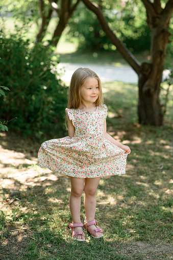 Little girl 3 years old in a summer sundress in the park. Summer time. The little girl clumsily lifted her dress