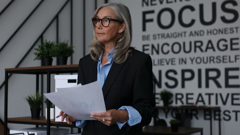 caucasian Middle aged older businesswoman with documents in her hands on the background of a modern office, News reporting office concept