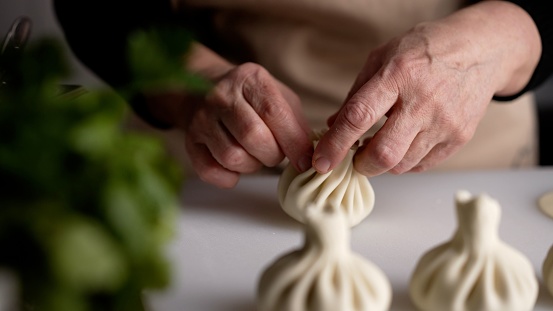Khinkali production. The chef's hands sculpt khinkali against the background of handmade cutting boards. Delicious homemade food, Georgian cuisine. Woman chef prepares khinkali in the restaurant kitchen.