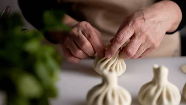 Khinkali production. The chef's hands sculpt khinkali against the background of handmade cutting boards. Delicious homemade food, Georgian cuisine. Woman chef prepares khinkali in the restaurant kitchen. stock photo