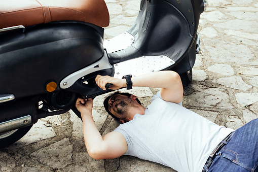 Young man having problems with the motorbike on the road. Man under the motorcycle trying to fix the problem of the motorcycle due to a breakdown. Road motorcycle insurance concept
