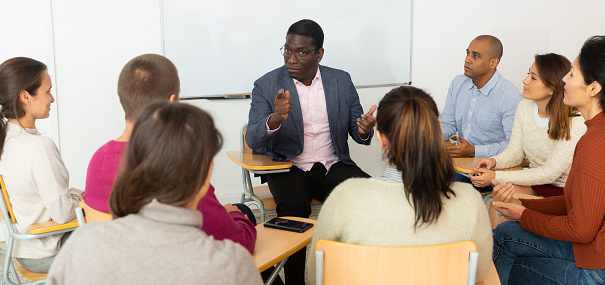 Multi-ethnic group of  adult people sitting in circle and sharing ideas during class in \n\ncollege