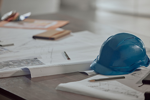 Building plans, blueprint and safety helmet for construction planning with tools, drawings and equipment on table. Documents, floor plan and industrial architecture paperwork for project strategy