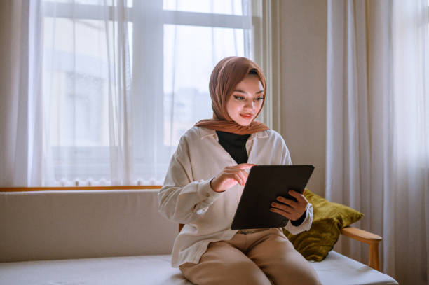 istock Young woman with hijab using digital tablet on couch at home 1472536160