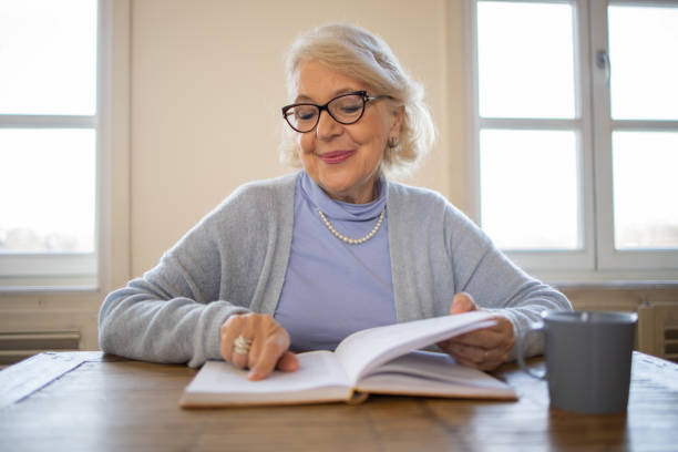 istock Senior woman reading book at home 1472538256