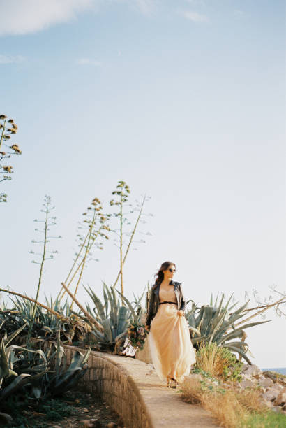 istock Bride in sunglasses walks along a stone curb past agave bushes 1472538341