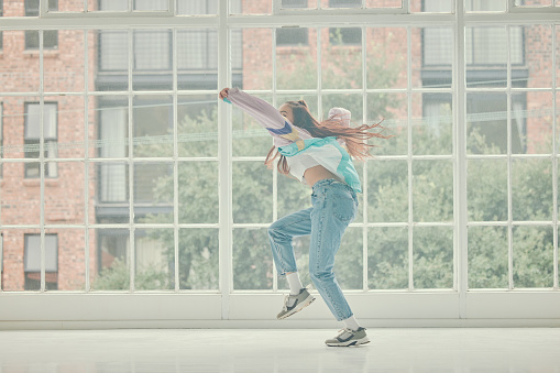Dance, trendy and hip hop with woman in studio for training, movement and expression. Creative, fitness and energy with girl dancing to music by window for artist, performance and breakdance