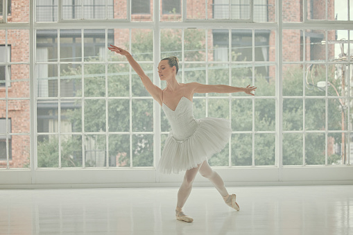 Ballet, woman and dancing at window for training, musical theatre and concert studio. Female ballerina, dancer and learning body performance, stage production and broadway academy of elegant position