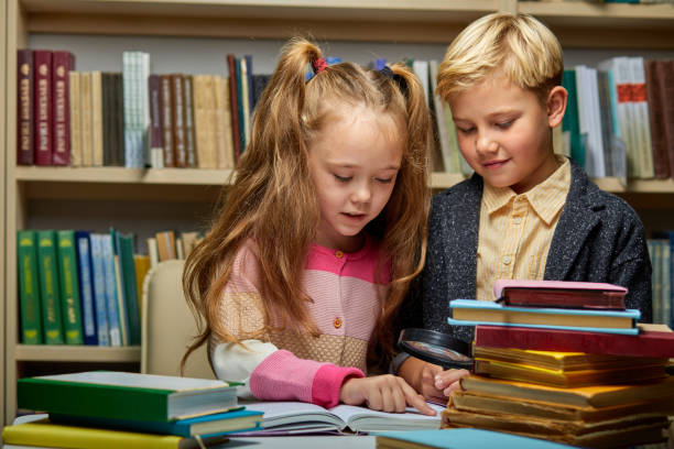 istock school kids reading book together while sitting at table in library 1472538760
