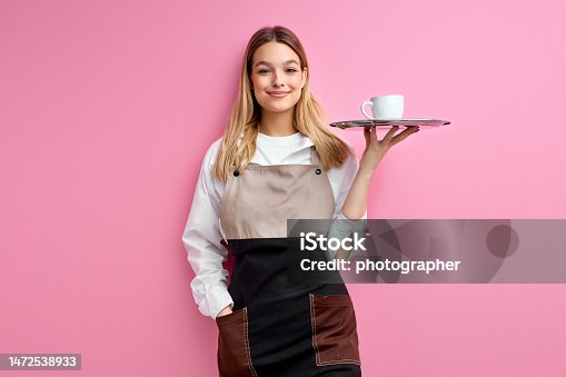 istock Stylish nice woman waitress in apron, offering cup of delicious tasty coffee 1472538933