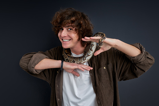 smiling guy stand brave with snake on him, caucasian male doesn't afraid of animals
